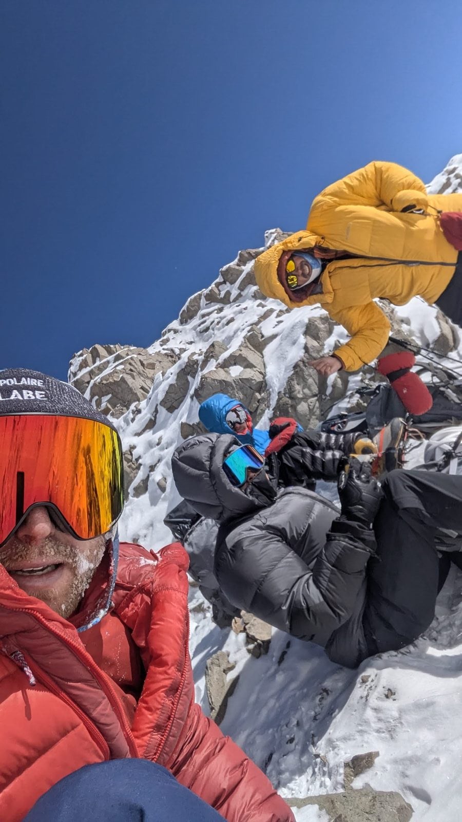 Climbers in heavy down jackets high on Aconcagua, frost on beards, rock and snow, deep blue sky