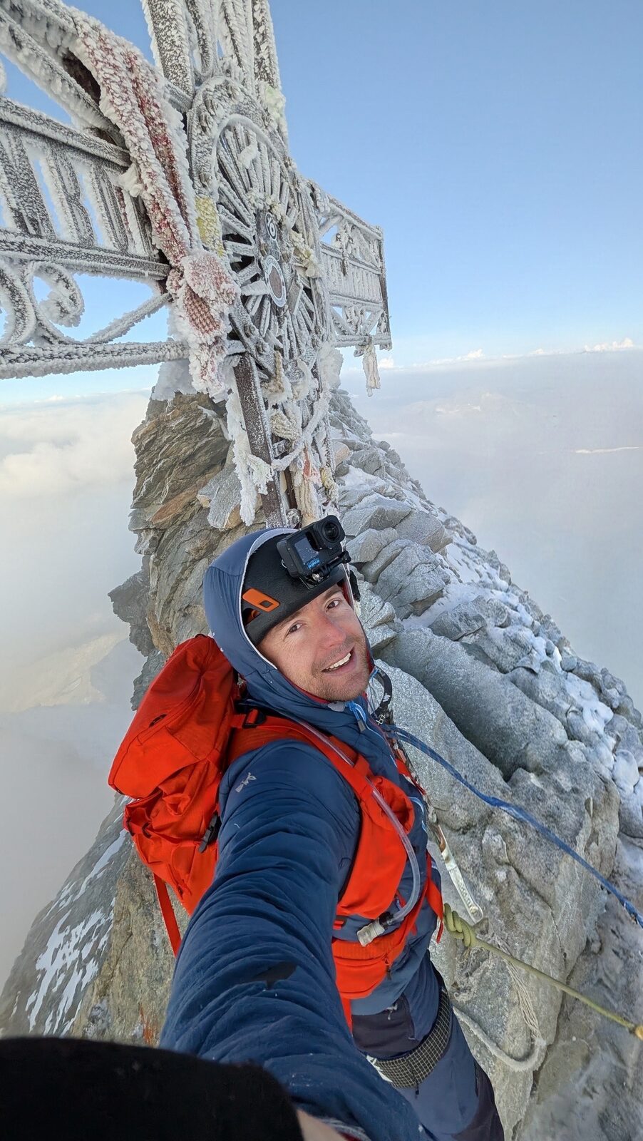 Sam at the rime-covered summit cross on the Matterhorn, the summit ridge and a sea of cloud below