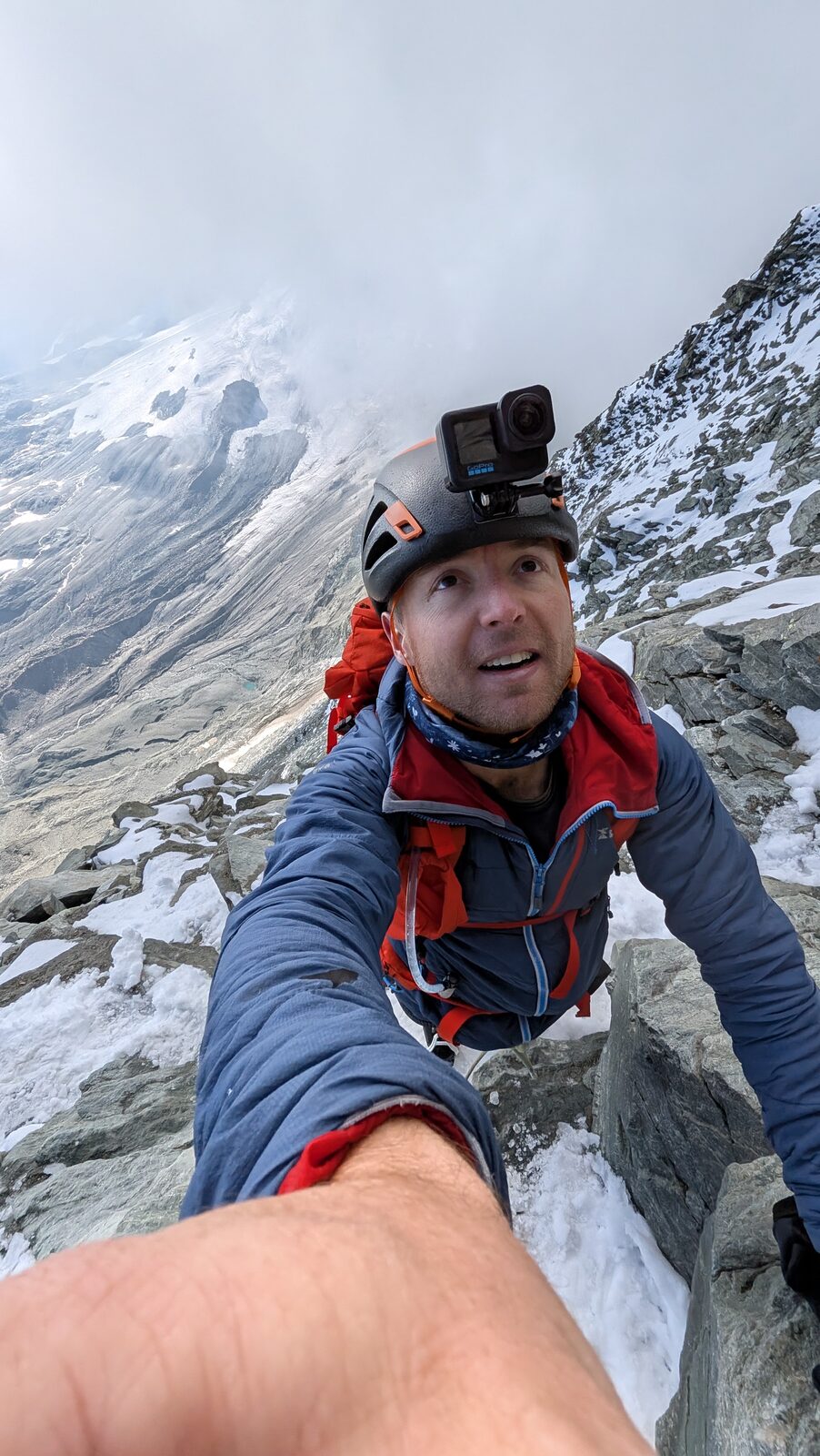 Sam climbing steep mixed rock and snow high on the Hörnli Ridge, GoPro on his helmet, the glacier far below